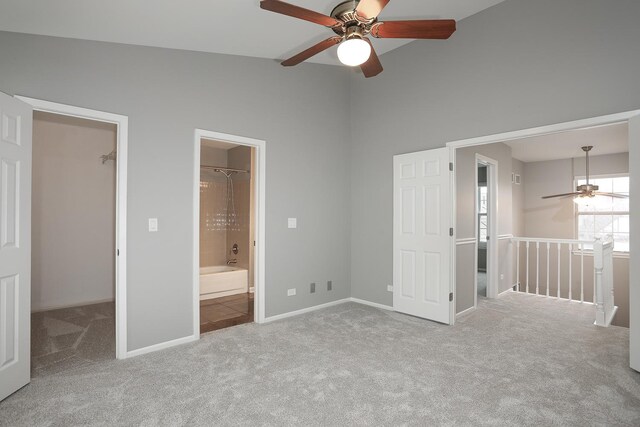 unfurnished bedroom with a walk in closet, carpet, baseboards, ensuite bathroom, and a ceiling fan