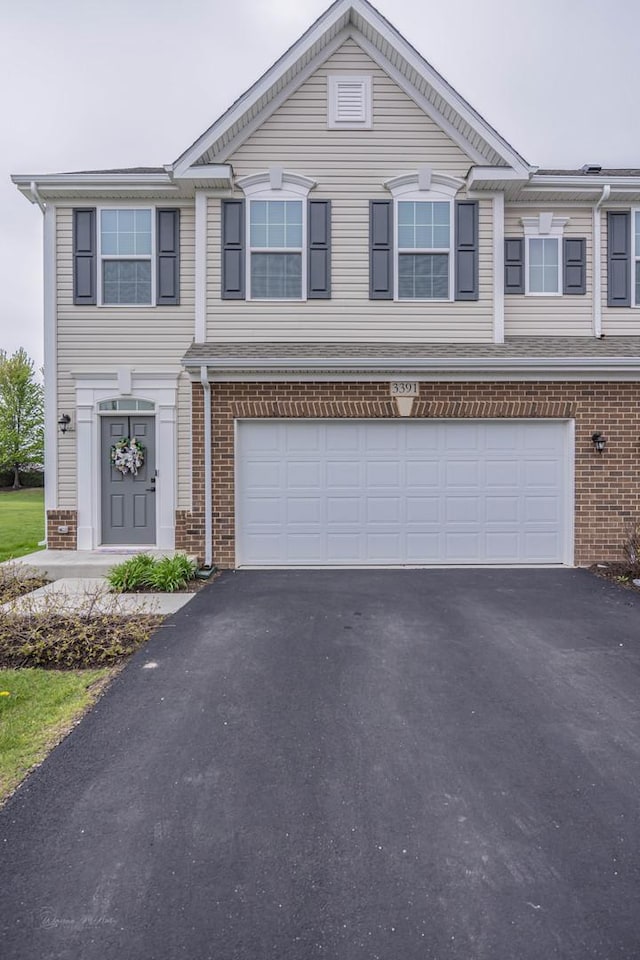 view of property featuring brick siding, driveway, and an attached garage