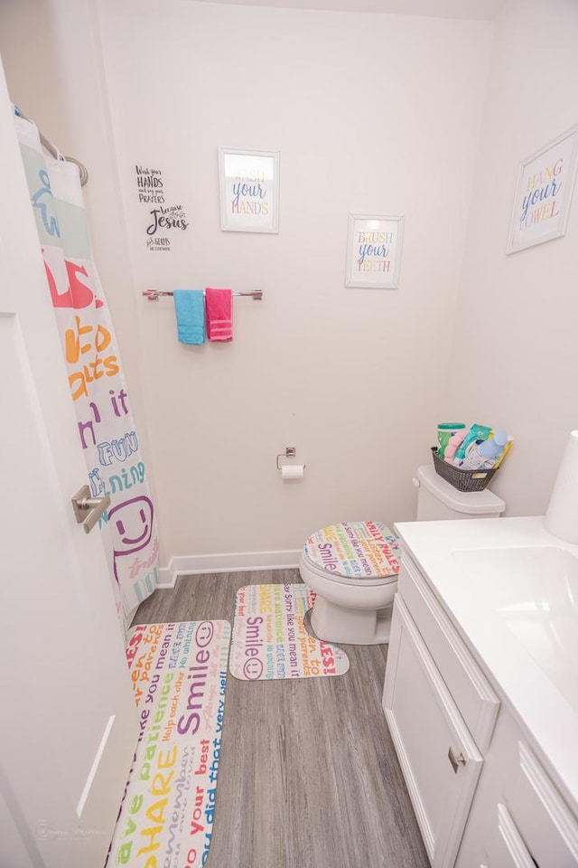 bathroom featuring wood finished floors, toilet, vanity, and baseboards