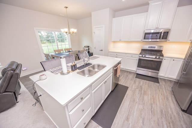 kitchen with appliances with stainless steel finishes, a sink, light wood finished floors, and a chandelier