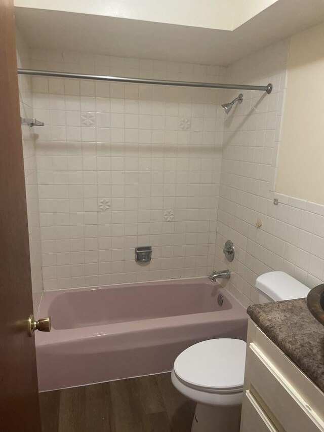 bathroom with wood finished floors, tile walls, toilet, shower / washtub combination, and vanity