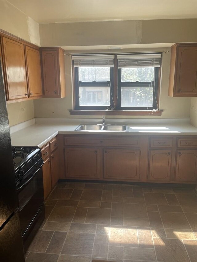 kitchen featuring black gas range oven, a sink, light countertops, and brown cabinets