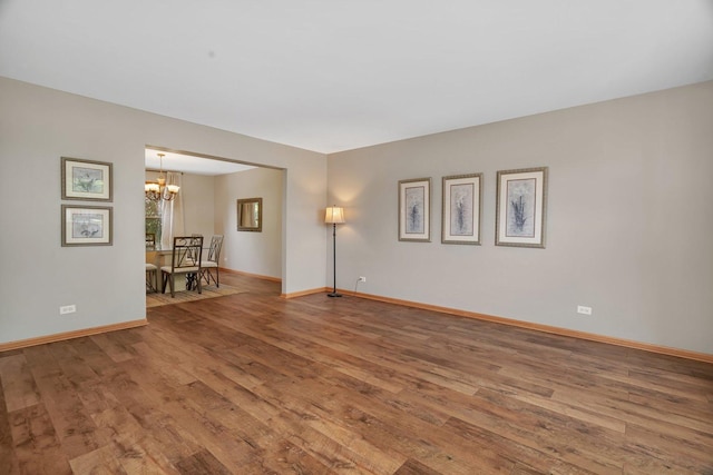 spare room with a chandelier, wood finished floors, and baseboards