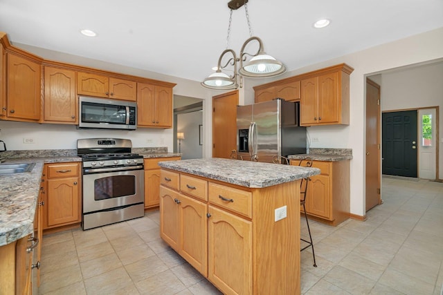 kitchen featuring appliances with stainless steel finishes, a center island, a sink, hanging light fixtures, and light tile patterned flooring
