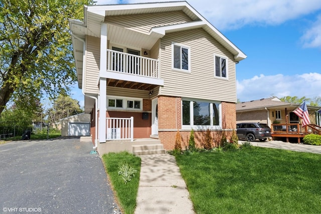 view of front of house featuring a balcony, brick siding, a detached garage, and a front lawn