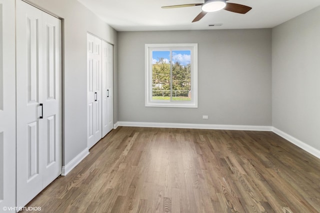 unfurnished bedroom with wood finished floors, two closets, baseboards, and ceiling fan