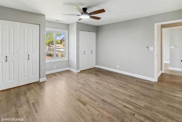 unfurnished bedroom featuring multiple closets, wood finished floors, baseboards, and ceiling fan