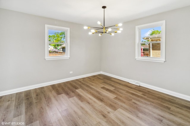 empty room with a chandelier, baseboards, and wood finished floors