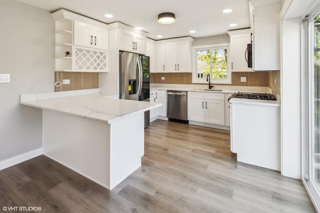 kitchen with stainless steel appliances, a sink, a peninsula, white cabinetry, and recessed lighting