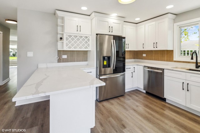 kitchen with appliances with stainless steel finishes, a peninsula, open shelves, a sink, and white cabinets