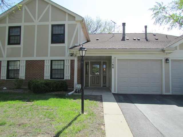 tudor home with brick siding, a garage, a front yard, and asphalt driveway