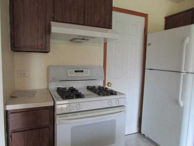 kitchen with white appliances, under cabinet range hood, light countertops, light tile patterned flooring, and dark brown cabinetry