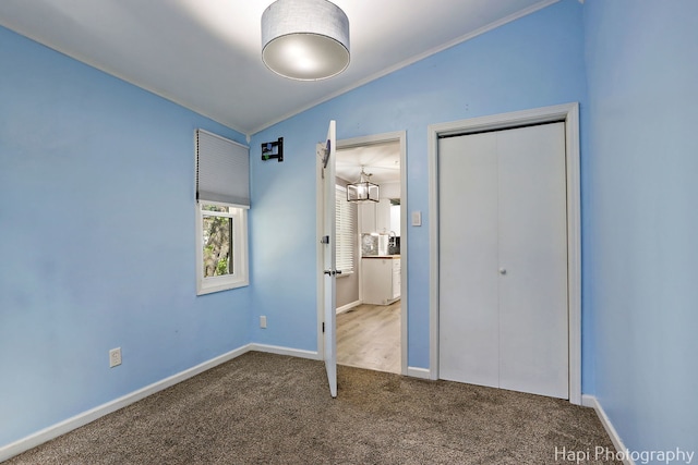 unfurnished bedroom featuring crown molding, carpet flooring, a closet, baseboards, and vaulted ceiling