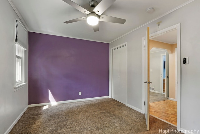 carpeted empty room with ceiling fan, baseboards, ornamental molding, and arched walkways