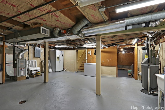 unfinished below grade area featuring white fridge with ice dispenser, electric panel, heating unit, and stairs