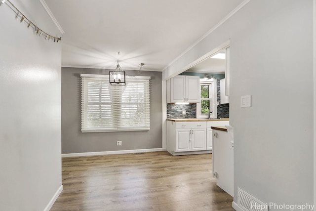 kitchen featuring ornamental molding, a chandelier, white cabinets, decorative backsplash, and light wood finished floors