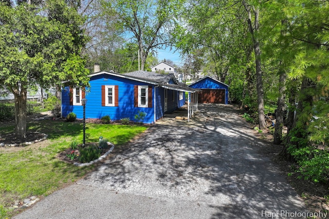 view of front of house with asphalt driveway, an outbuilding, a front lawn, and a chimney