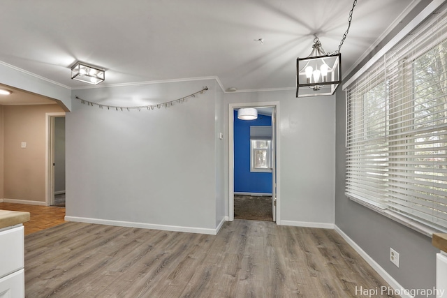 empty room featuring ornamental molding, a chandelier, wood finished floors, and baseboards