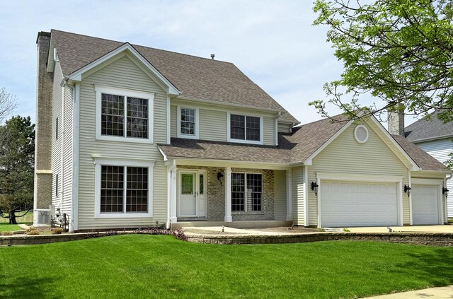 traditional-style house with a front yard, an attached garage, a shingled roof, and driveway