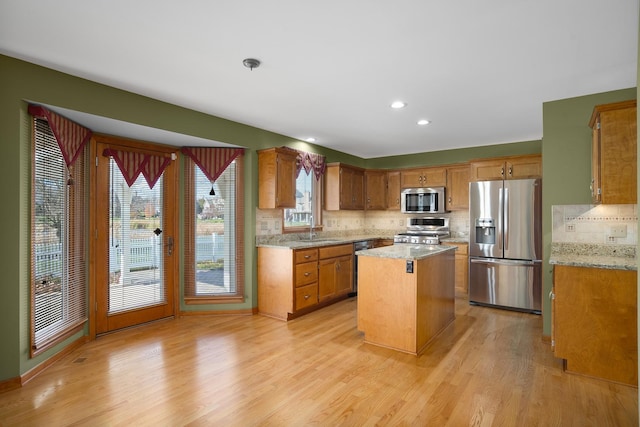 kitchen featuring appliances with stainless steel finishes, backsplash, light wood-style flooring, brown cabinets, and a sink