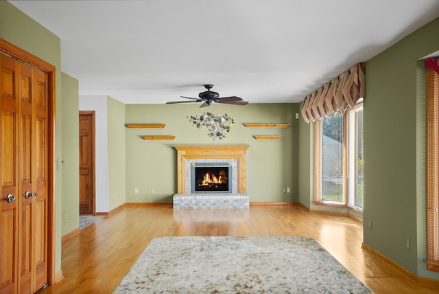 unfurnished living room featuring light wood finished floors, a fireplace, ceiling fan, and baseboards