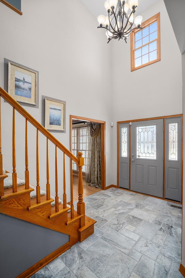 entrance foyer featuring a chandelier, a towering ceiling, stairway, stone tile flooring, and baseboards