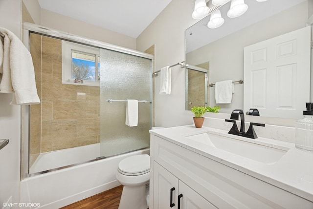 full bath featuring toilet, vanity, wood finished floors, and shower / bath combination with glass door