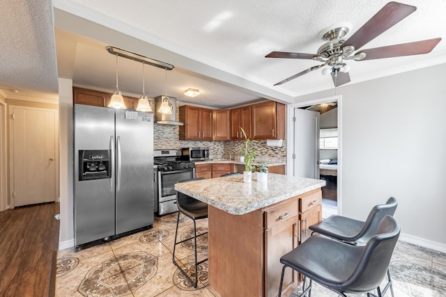 kitchen with appliances with stainless steel finishes, wall chimney exhaust hood, a kitchen bar, light countertops, and tasteful backsplash