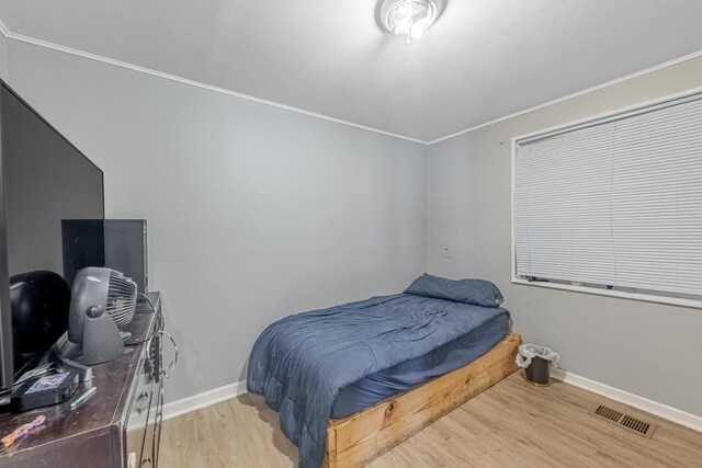 bedroom with wood finished floors, baseboards, and ornamental molding