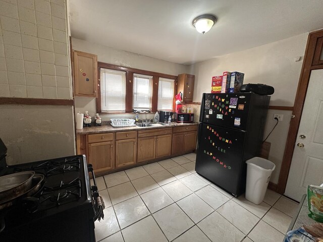 kitchen featuring black appliances, brown cabinets, light tile patterned floors, and a sink