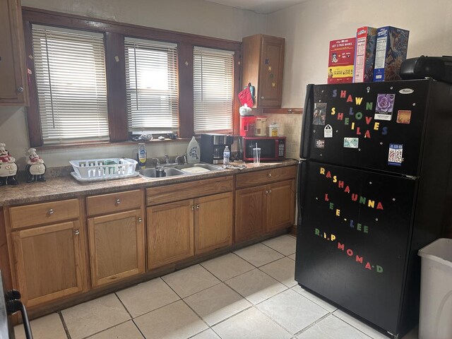kitchen with freestanding refrigerator, a sink, light tile patterned flooring, and brown cabinetry