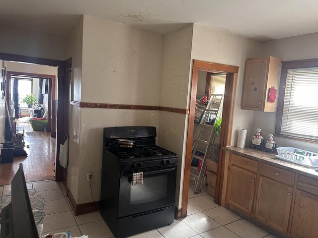 kitchen with black gas range oven, light tile patterned flooring, electric panel, and brown cabinets
