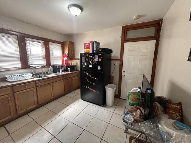 kitchen with freestanding refrigerator, a sink, brown cabinets, and light tile patterned flooring