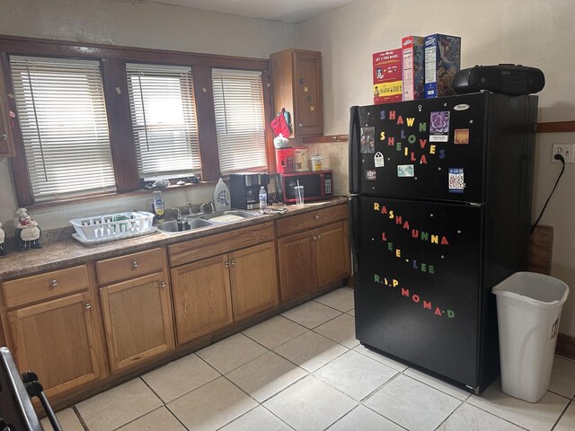 kitchen featuring freestanding refrigerator, a sink, light tile patterned flooring, and brown cabinetry