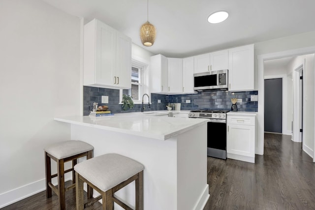 kitchen with appliances with stainless steel finishes, a peninsula, a breakfast bar, and white cabinetry
