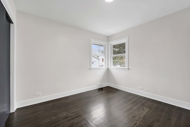 spare room with baseboards and dark wood-type flooring