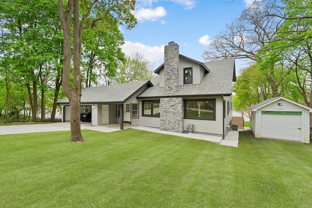view of front facade with a shingled roof, an outdoor structure, a chimney, concrete driveway, and a front yard
