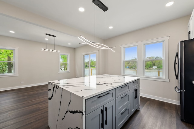 kitchen featuring freestanding refrigerator, gray cabinets, baseboards, a kitchen island, and light stone counters