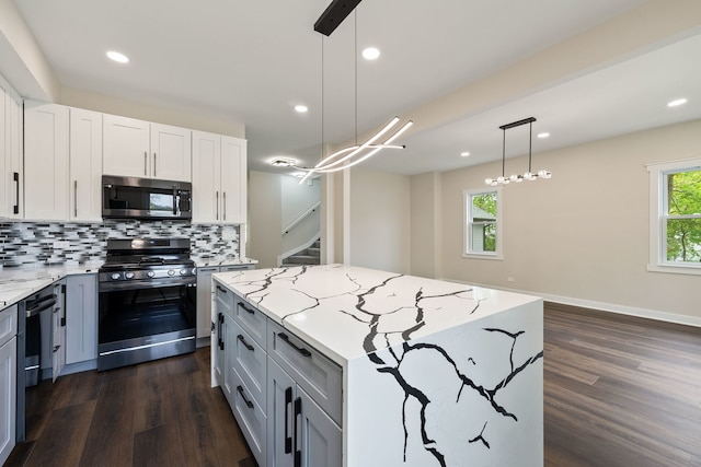 kitchen with appliances with stainless steel finishes, dark wood-style floors, a center island, light stone counters, and recessed lighting