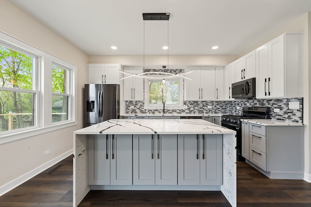 kitchen with black appliances, a center island, tasteful backsplash, light stone countertops, and baseboards