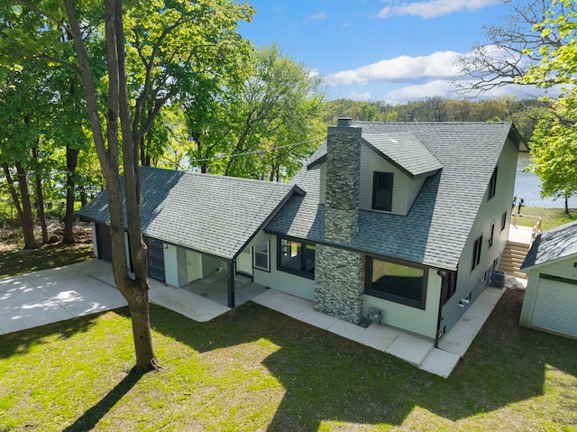 rear view of property featuring a chimney, driveway, roof with shingles, and a lawn