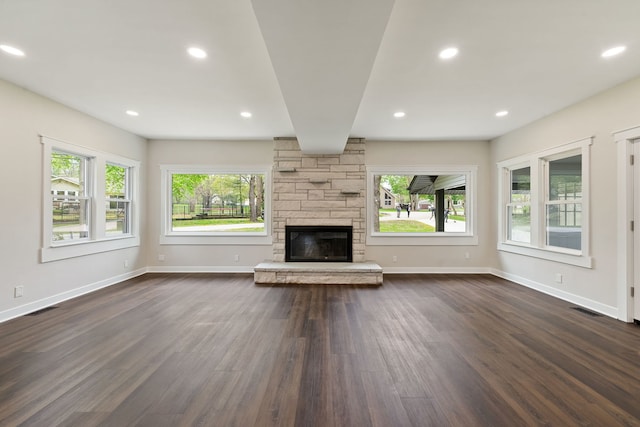 unfurnished living room featuring plenty of natural light, dark wood-style floors, baseboards, recessed lighting, and a stone fireplace