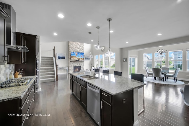 kitchen with stainless steel appliances, wall chimney exhaust hood, plenty of natural light, a stone fireplace, and recessed lighting