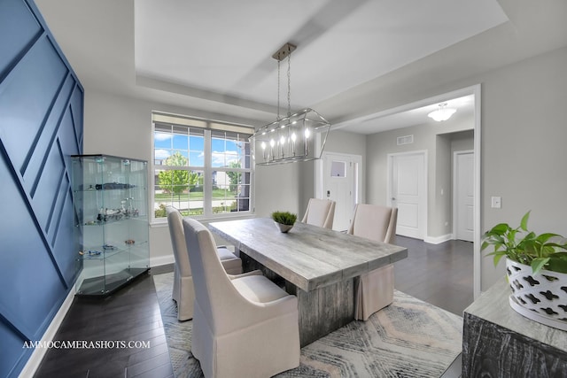 dining area featuring dark wood-type flooring, baseboards, a chandelier, and a raised ceiling