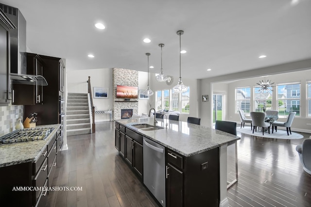 kitchen featuring stainless steel appliances, wall chimney range hood, a fireplace, plenty of natural light, and recessed lighting