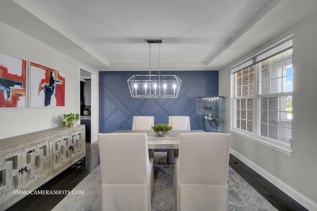 dining space with a chandelier, an accent wall, a raised ceiling, wood finished floors, and baseboards