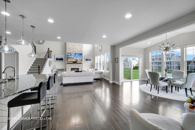 living room with stairs, a stone fireplace, lofted ceiling, dark wood-style floors, and baseboards
