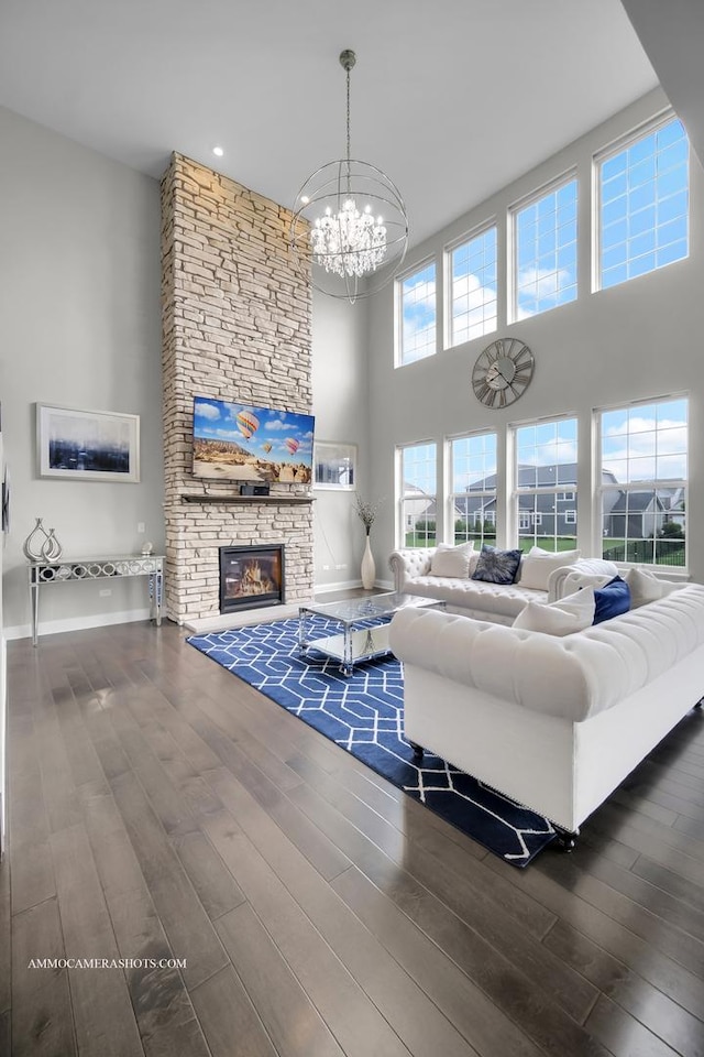 living room featuring a towering ceiling, a chandelier, a stone fireplace, wood finished floors, and baseboards