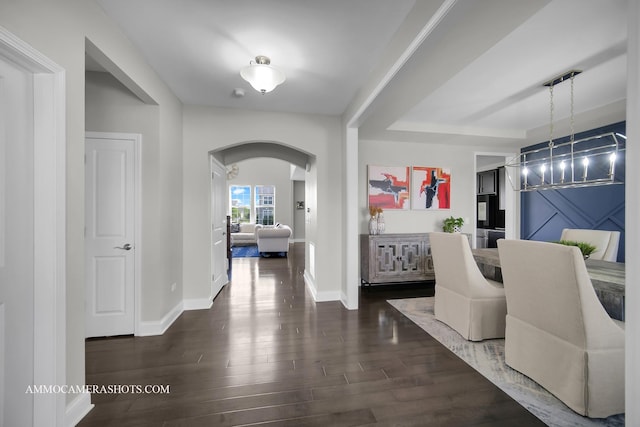 corridor with arched walkways, wood finished floors, and baseboards