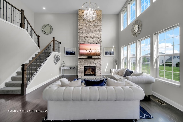 living room with a towering ceiling, baseboards, hardwood / wood-style flooring, a chandelier, and a fireplace